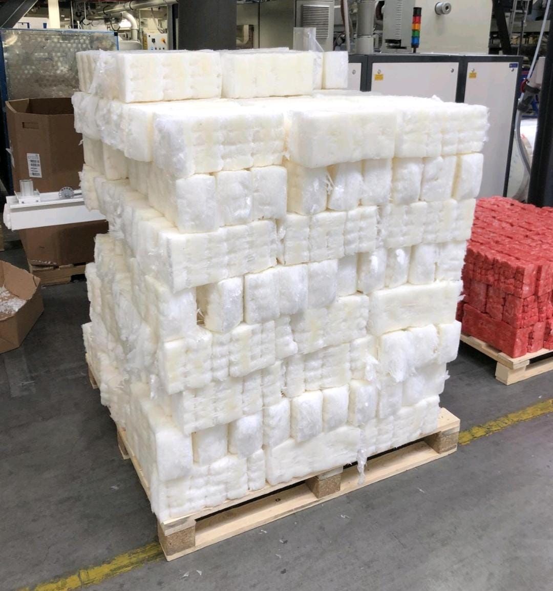 Palette mit gestapelten, verdichteten Stangen aus Folienabfall in einer Produktionshalle